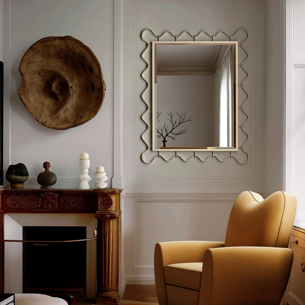 Lemieux et Cie brass mirror with scalloped frame in antique finish, hung above carved mantel with sculptural objects in neutral paneled sitting room.