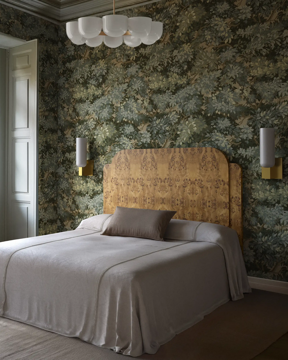 Lemieux et Cie Maroux wall sconce in burnished brass and aged iron with vertical opal glass illumination, styled in a bedroom with the Avenire bed, Verdure wallpaper, and the Cheverny chandelier.