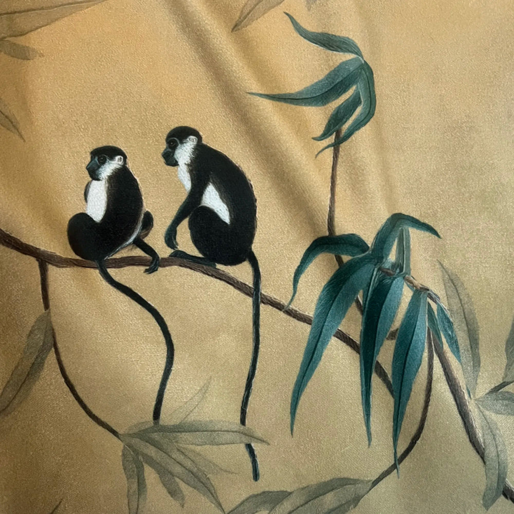 Lemieux et Cie Les Singes Velvet Pillow in gold with black and white monkeys and teal bamboo motif, decorative pillow shown draped with soft light.