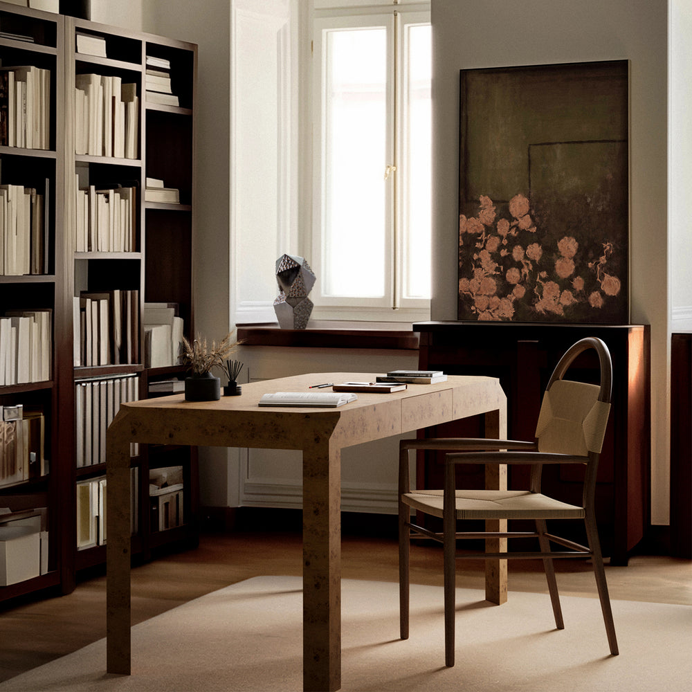 Lemieux et Cie Armand Desk in hand-matched burl veneer, angular writing desk in a study with dark shelving, neutral walls, and soft daylight.