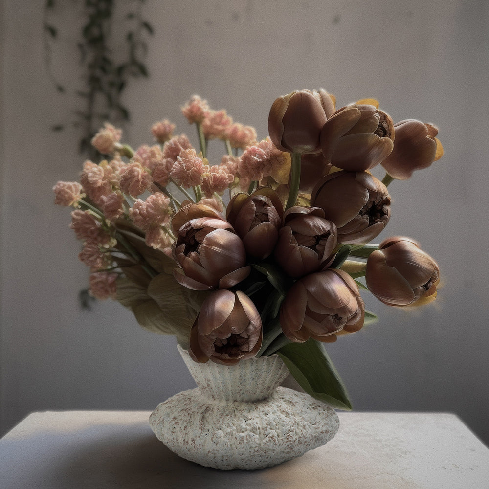 Lemieux et Cie Vilette Vase, textural ceramic vessel with organic sculptural form, styled with warm tulips and blush florals on neutral surface.