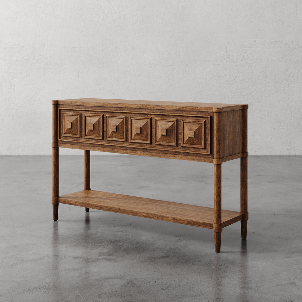 Lemieux et Cie Voltaire Console Table in warm wood with geometric faceted drawer fronts and lower shelf, shown on polished concrete floor against white plaster wall.