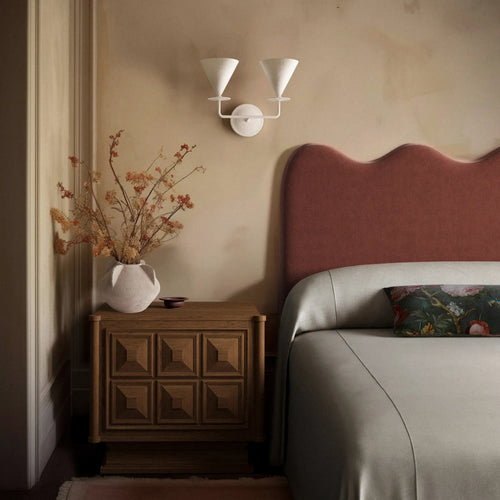 Lemieux et Cie Roanne Rug in natural wool, hand-knotted shag rug beside a nightstand with curved headboard in warm bedroom setting.