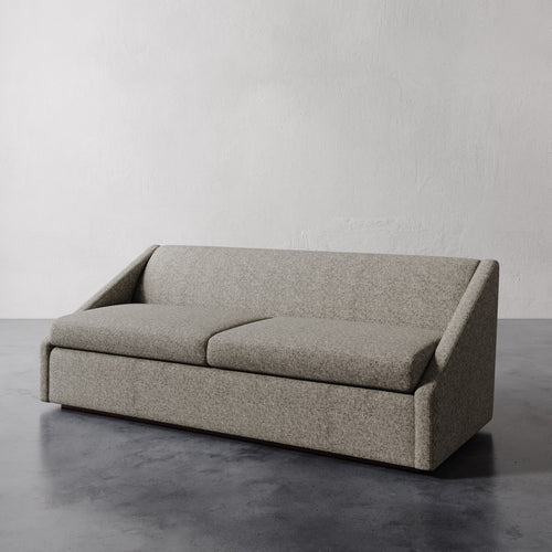 Lemieux et Cie Fontaine Sofa in warm grey upholstery, sofa with architectural silhouette and angled arms, shown on concrete floor against white plaster wall.