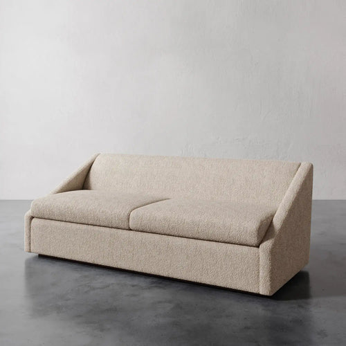 Lemieux et Cie Fontaine Sofa in ivory bouclé upholstery, low-profile sofa with angular arms, shown on polished concrete floor against textured plaster wall.