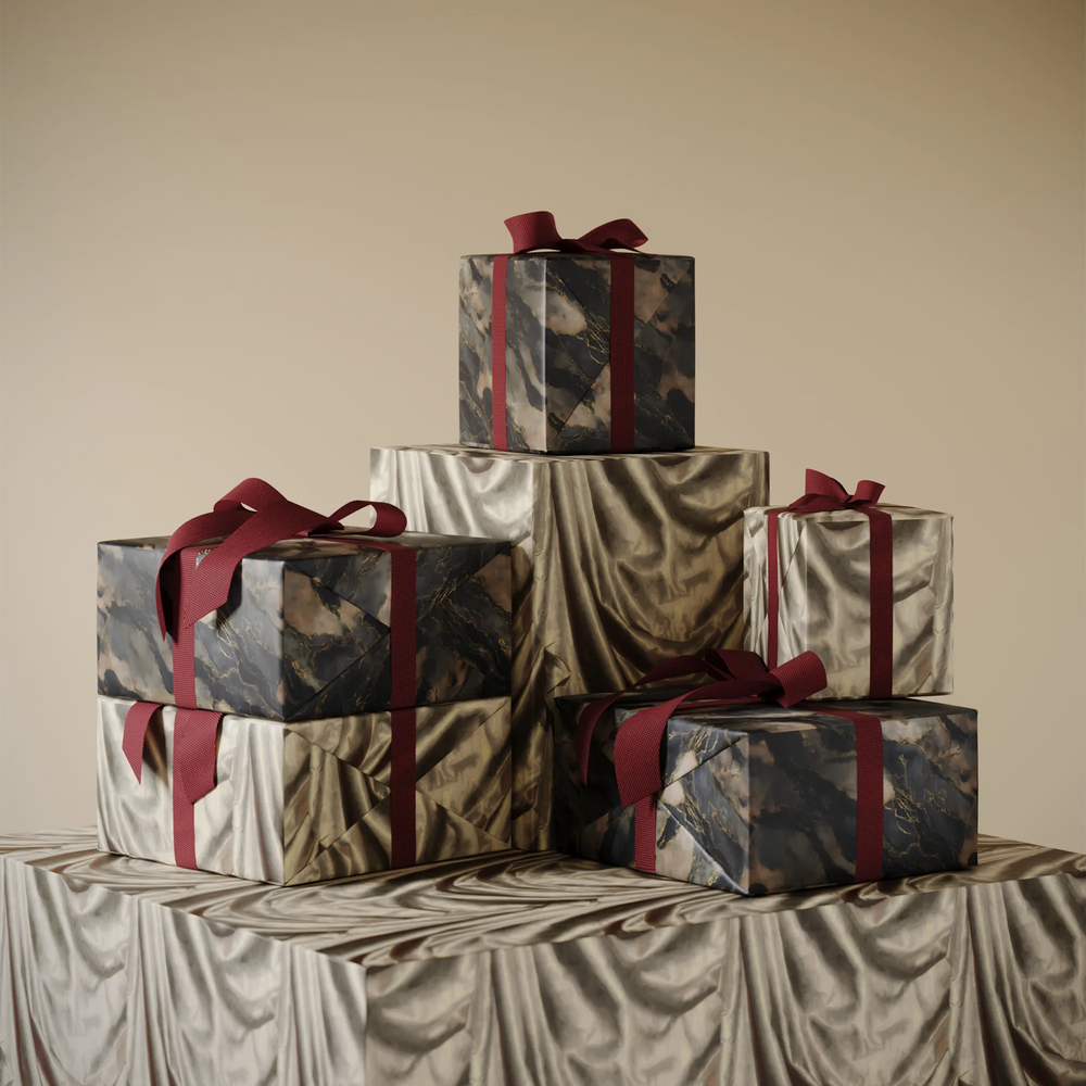 Lemieux et Cie gift wrapping paper in marbled and draped satin patterns with deep red ribbon, stacked on draped surface against neutral walls.