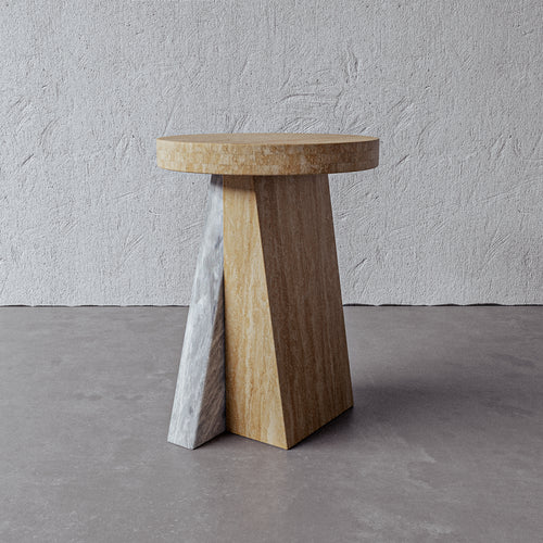 Lemieux et Cie Borel Side Table in walnut finish, sculptural side table with geometric angled base and round top, shown on concrete floor against textured plaster wall.