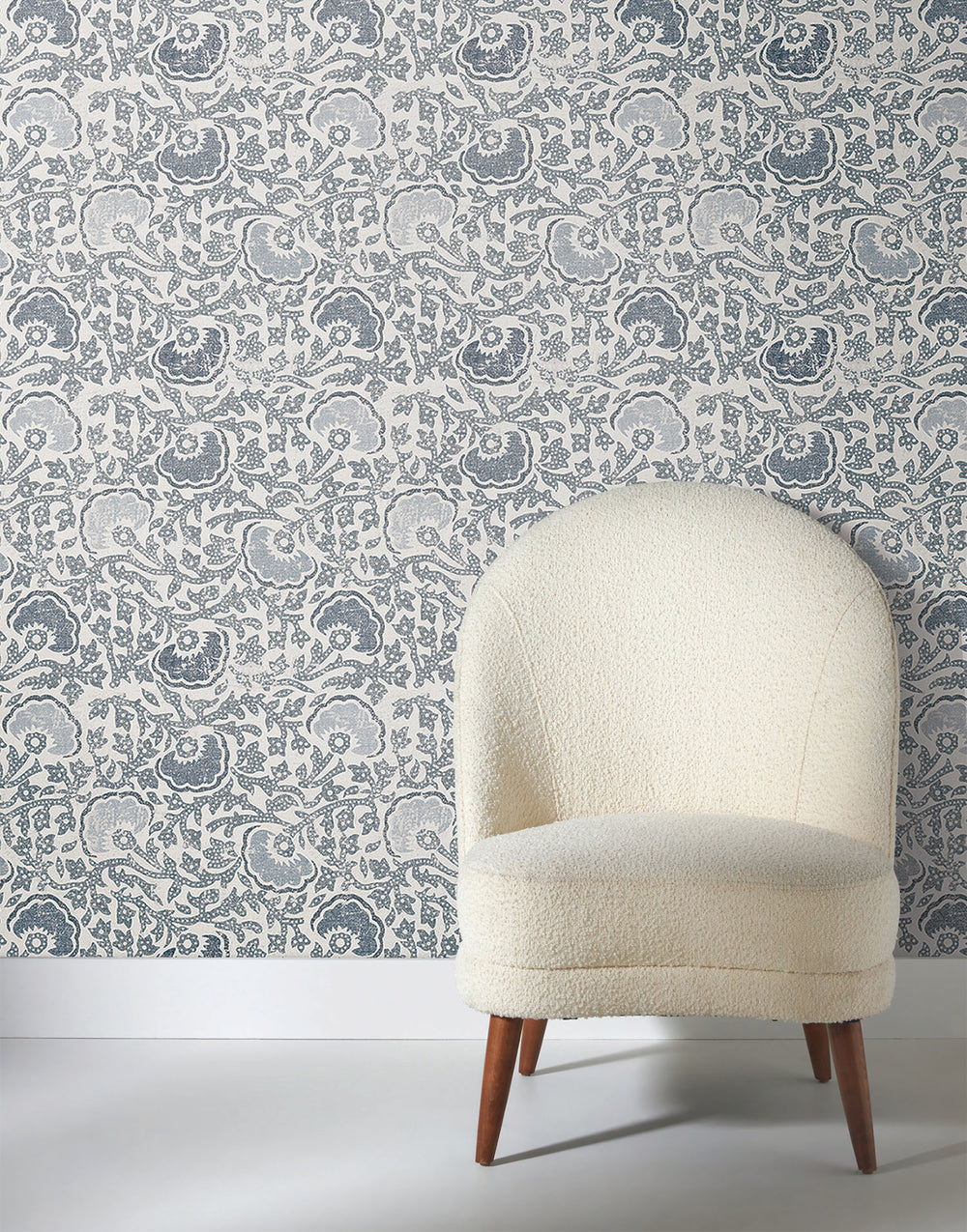 Lemieux et Cie sculptural side table in plaster with natural ivory coloring, angular form shown against blue-gray floral patterned wallpaper with white baseboards.