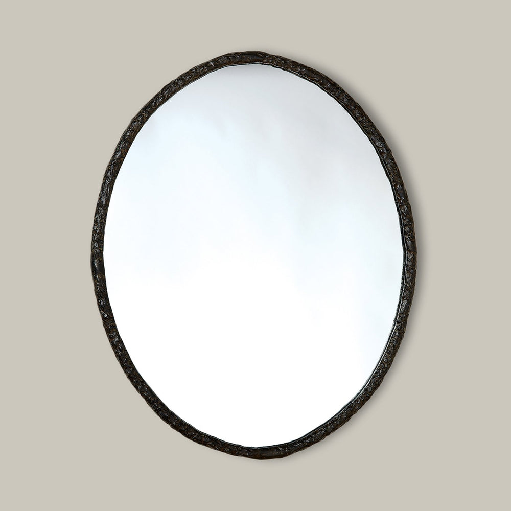 Lemieux et Cie Berger Mirror, oval form with textured dark frame, hung on neutral plaster wall in soft daylight.