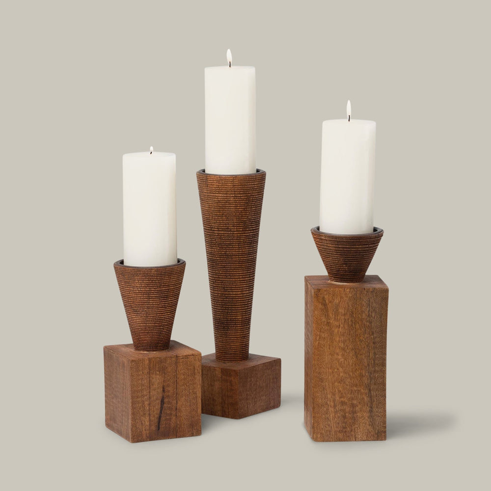 Lemieux et Cie handcrafted candleholder trio with textured tapered forms on wood block pedestals, sculptural pillar candles lit against neutral backdrop.