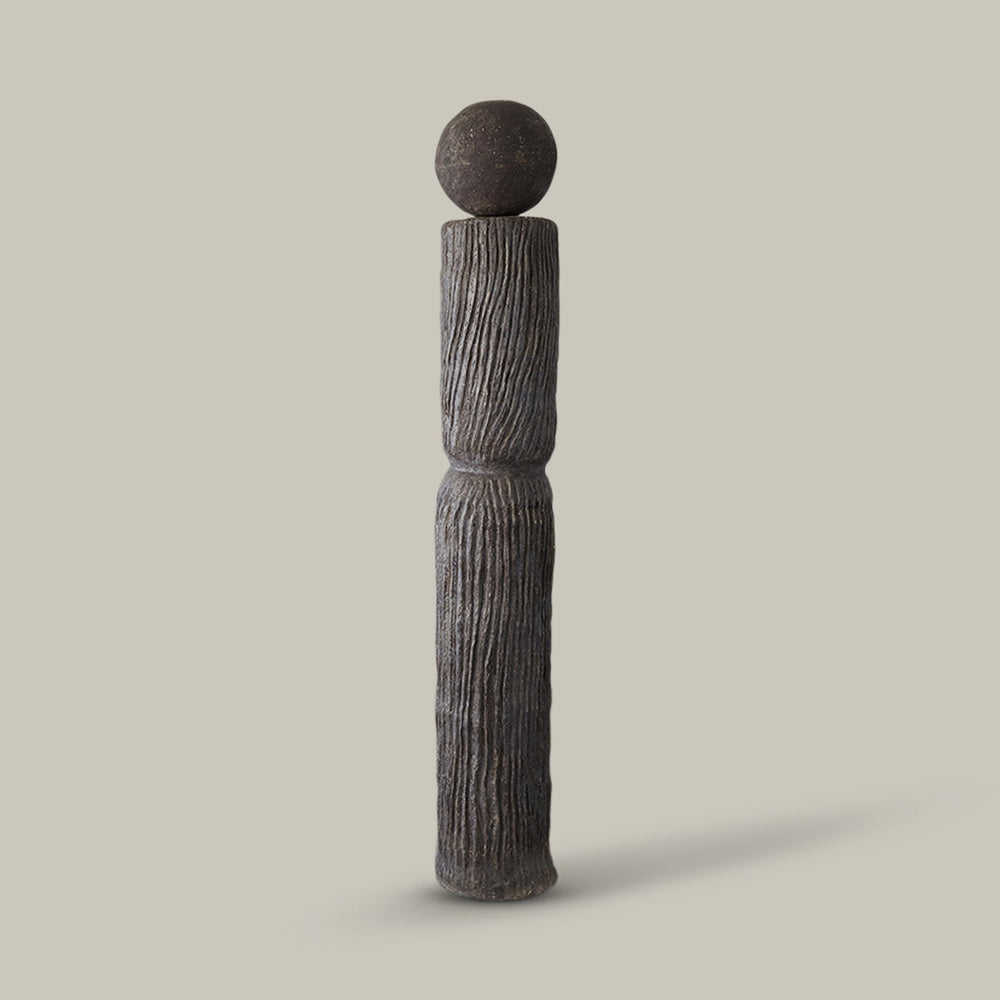 Lemieux et Cie Andre Totem, sculptural dark stone form with vertical ridged texture and sphere finial, shown on neutral studio backdrop.