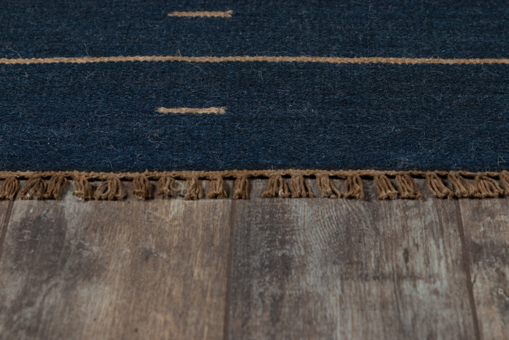 Lemieux et Cie Doukkala Rug in deep navy with camel striping, hand-knotted wool with fringe detail, shown on weathered wood floors.