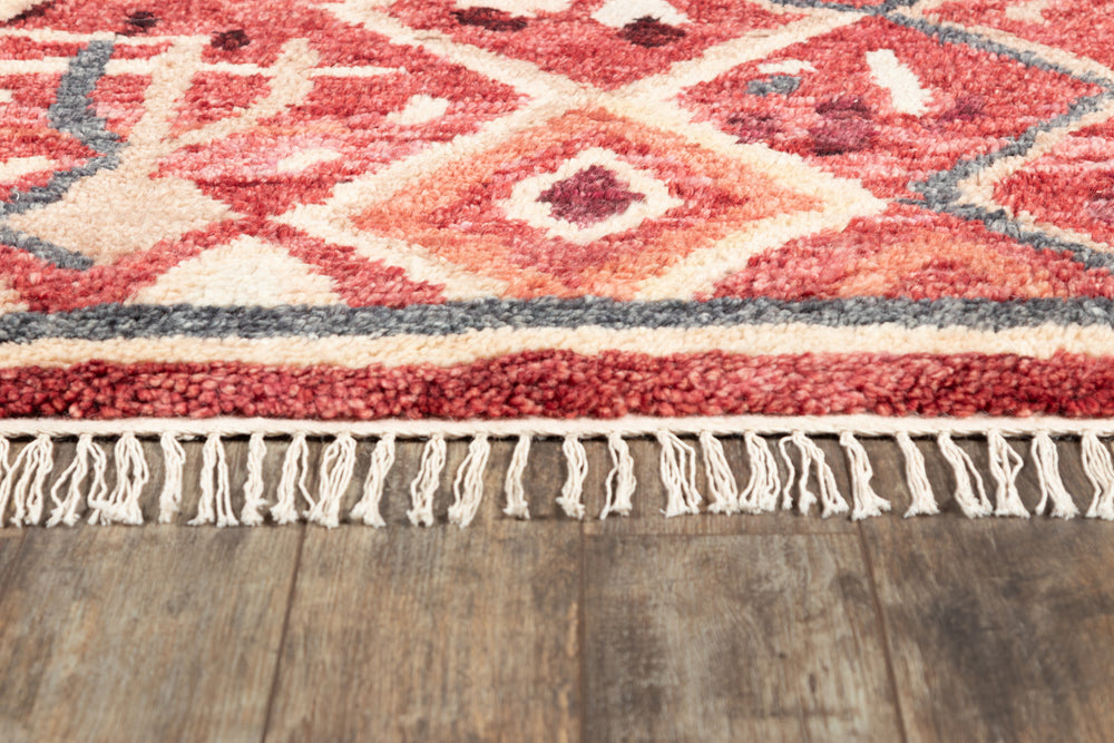 Lemieux et Cie Duar rug in coral and charcoal geometric pattern, handwoven with ivory fringe edge, shown on warm wood flooring.