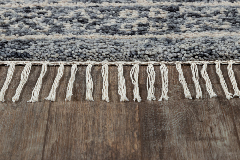 Lemieux et Cie Doukkala rug in charcoal and ivory handwoven wool, detail of knotted fringe edge on weathered wood flooring.