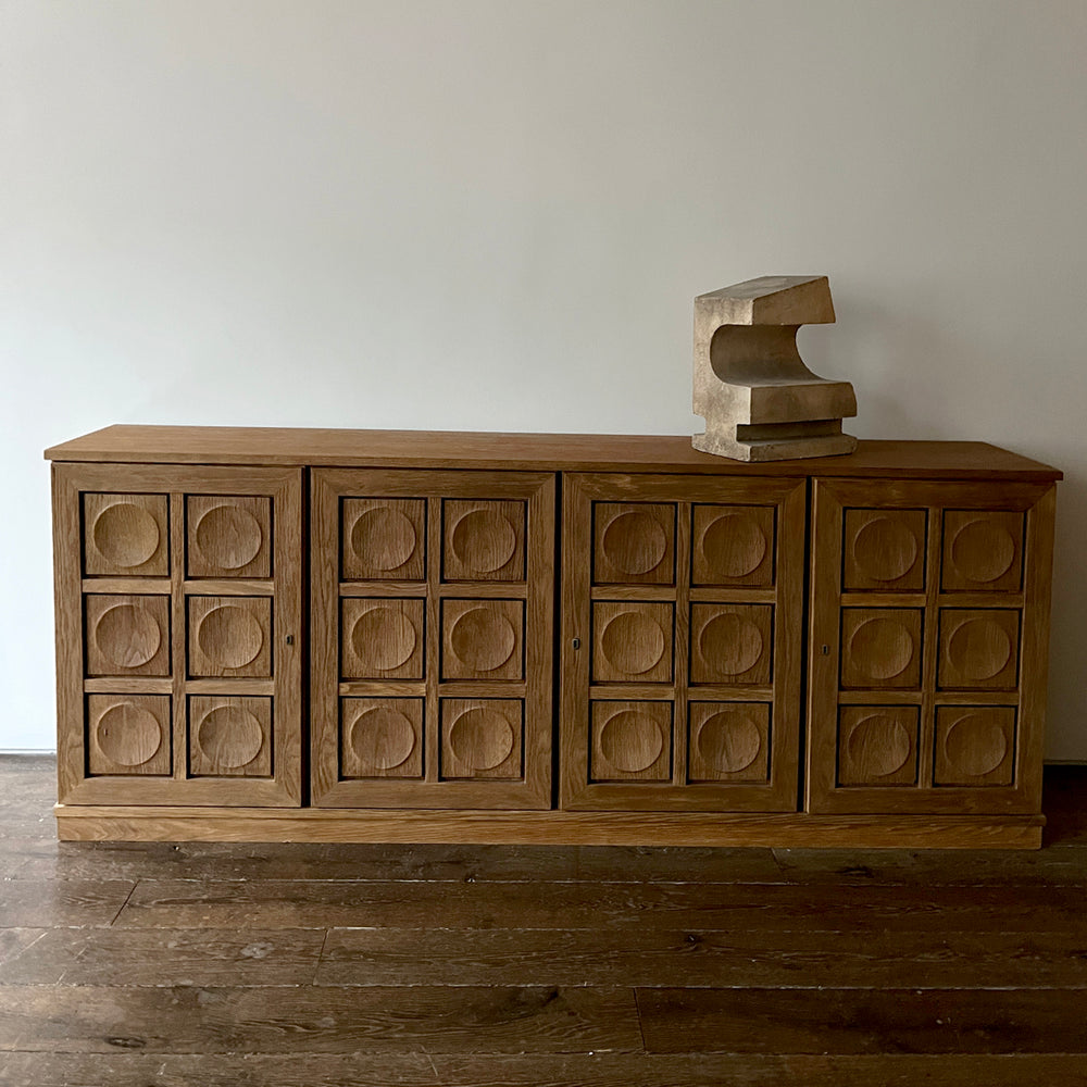 Lemieux et Cie platform sofa in cerused European oak with geometric circle-paneled doors, sculptural stone accent on top, aged wood floors and neutral walls.