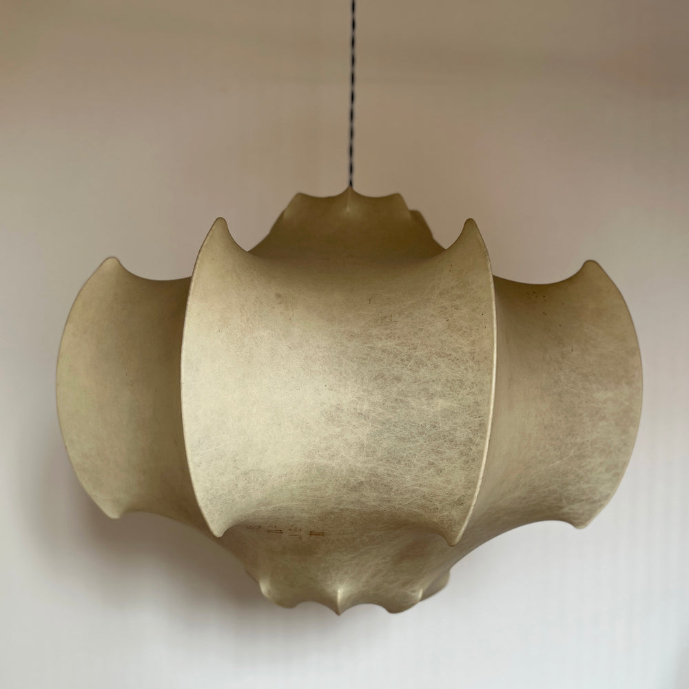 Lemieux et Cie Fontaine pendant light, sculptural layered shade with scalloped edges, suspended in a room with neutral plaster walls and warm ambient light.