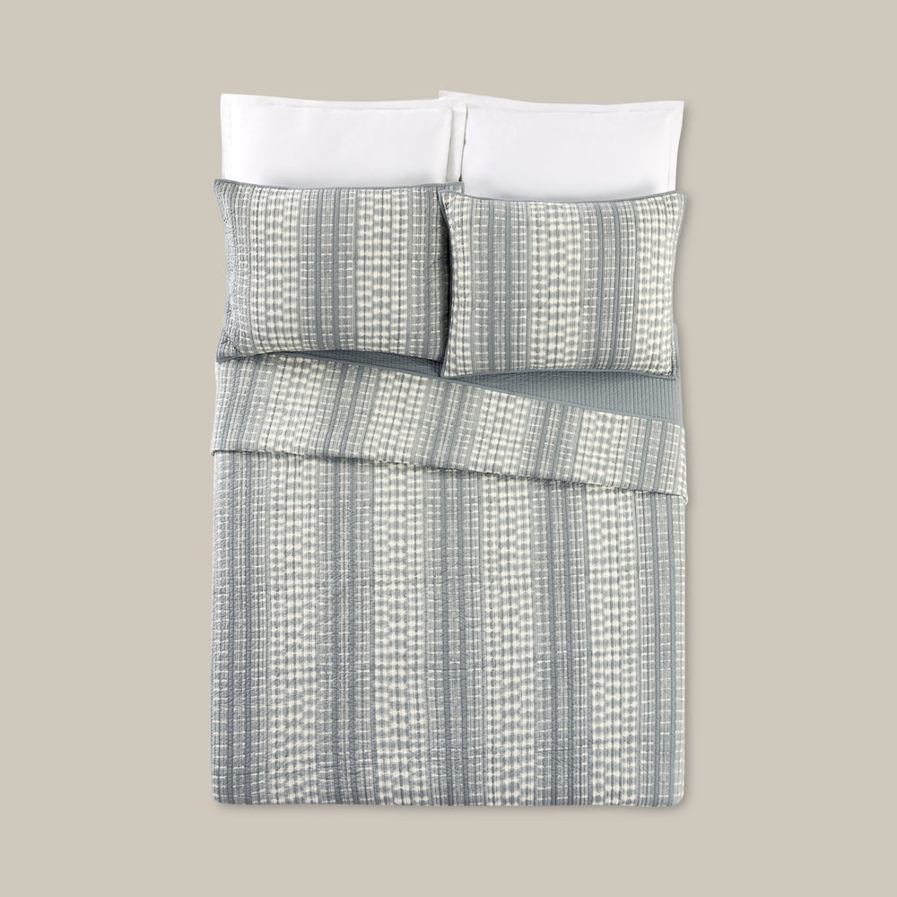 Lemieux et Cie Jepara Quilt Collection in cream cotton with tonal striped pattern, quilt and shams layered with white bedding on neutral backdrop.