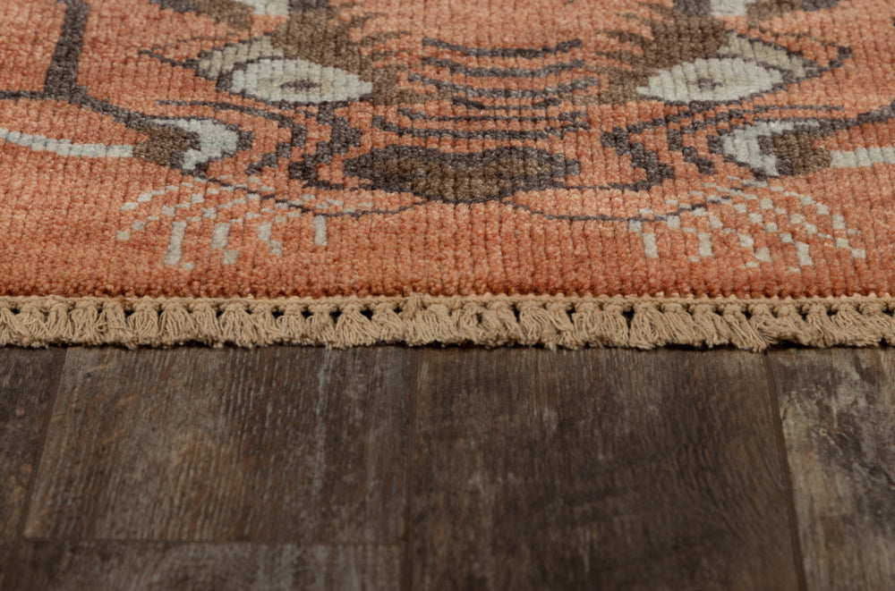 Lemieux et Cie Kouang rug in terracotta, sage and brown hand-knotted wool, close detail of fringe and traditional pattern on aged wood floor.