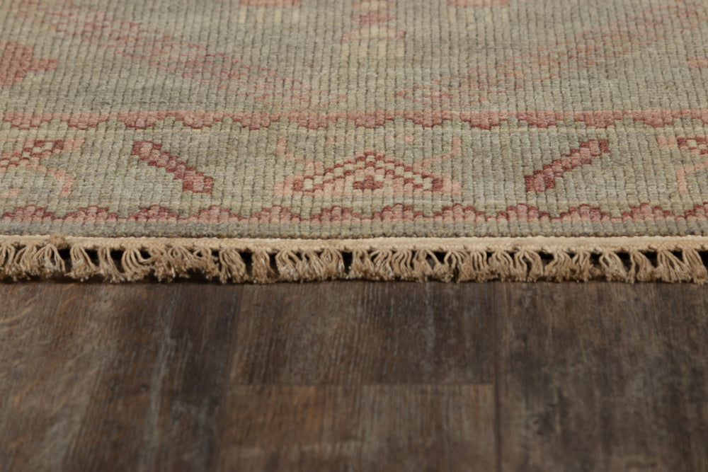 Lemieux et Cie Kouang rug in sage and rose, hand-knotted wool with fringed edge, shown on dark wood flooring.