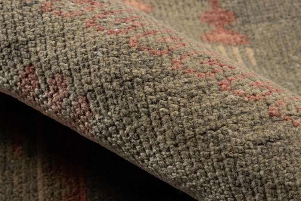 Lemieux et Cie Kouang rug in sage and blush handwoven wool, close detail of low pile and woven pattern edge against dark surface.