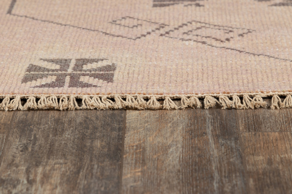 Lemieux et Cie Kouang rug in neutral tones with geometric motif, hand-knotted wool with fringe edge detail, shown on weathered wood flooring.