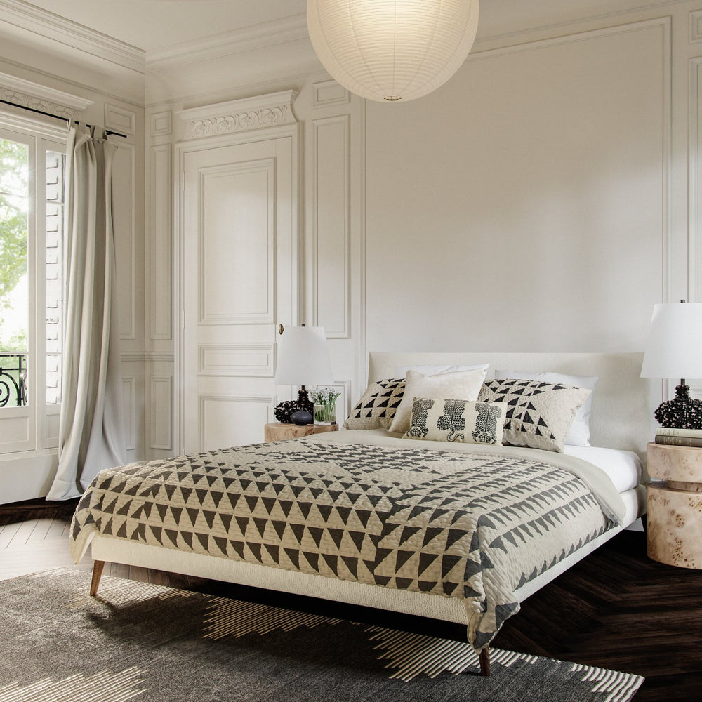 Lemieux et Cie Aubert Quilt Collection with graphic geometric pattern in neutral tones, quilt styled on upholstered bed in Parisian bedroom with paneled walls and dark wood floors.