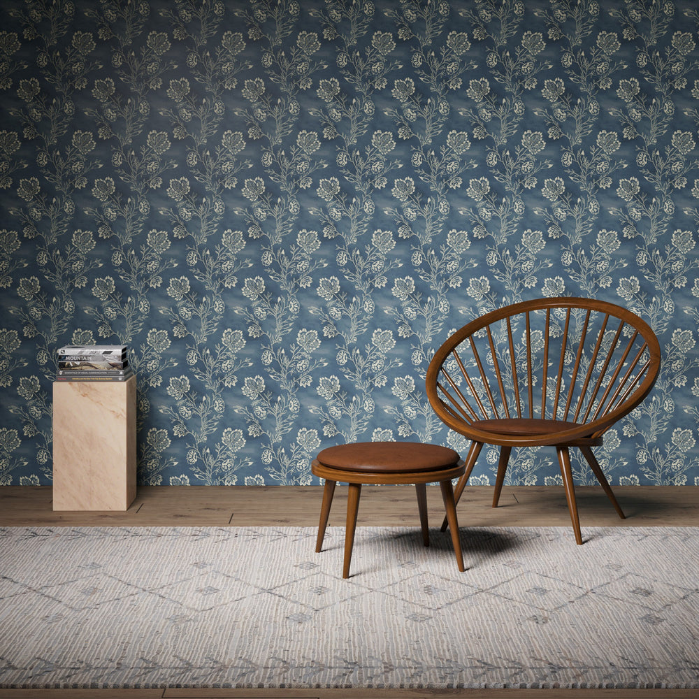 Lemieux et Cie side table with black ebonized base and honed travertine top, shown against blue floral wallpaper with leather chair and ottoman on patterned rug.