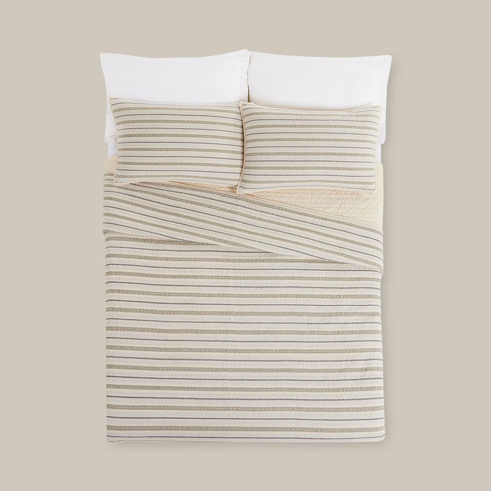 Lemieux et Cie Lucien Quilt in natural with taupe stripes, hand-painted textile bedding styled with white pillows on neutral backdrop.