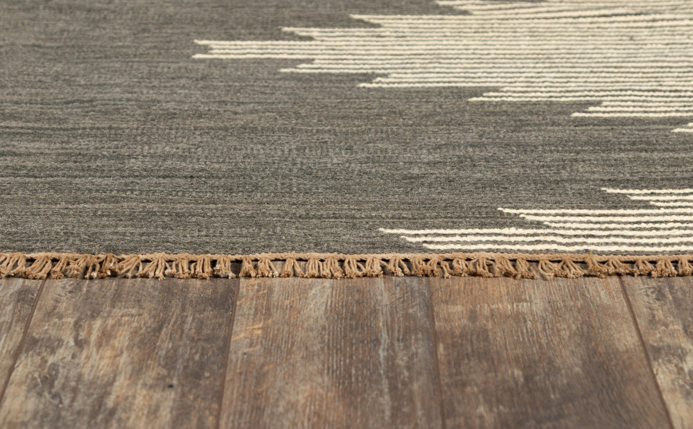 Lemieux et Cie Metlili rug in charcoal and ivory handwoven wool, detail showing fringed edge and geometric pattern on weathered wood flooring.