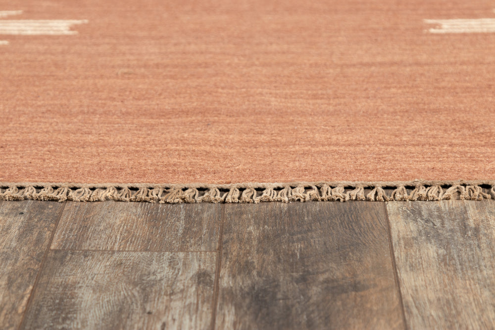 Lemieux et Cie Metlili rug detail in warm terra-cotta, handwoven wool with knotted fringe, shown on weathered wood flooring.
