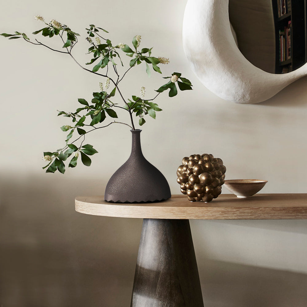 Lemieux et Cie Noelle Geometric Vase in black, sculptural ceramic vessel with fluted bottom, styled on wood console with round mirror and neutral walls.