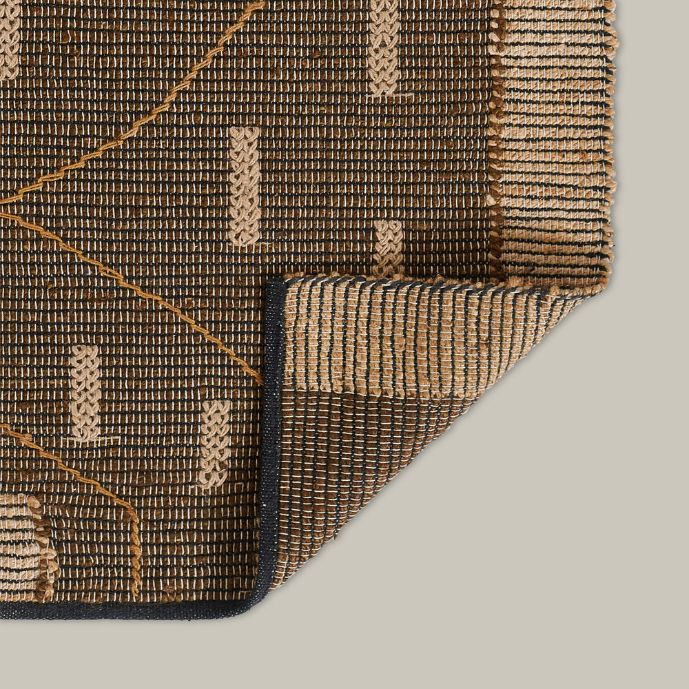 Lemieux et Cie Lemieux et Gie handwoven rug in charcoal and natural with geometric pattern, flatweave textile shown folded to reveal reverse side on neutral backdrop.