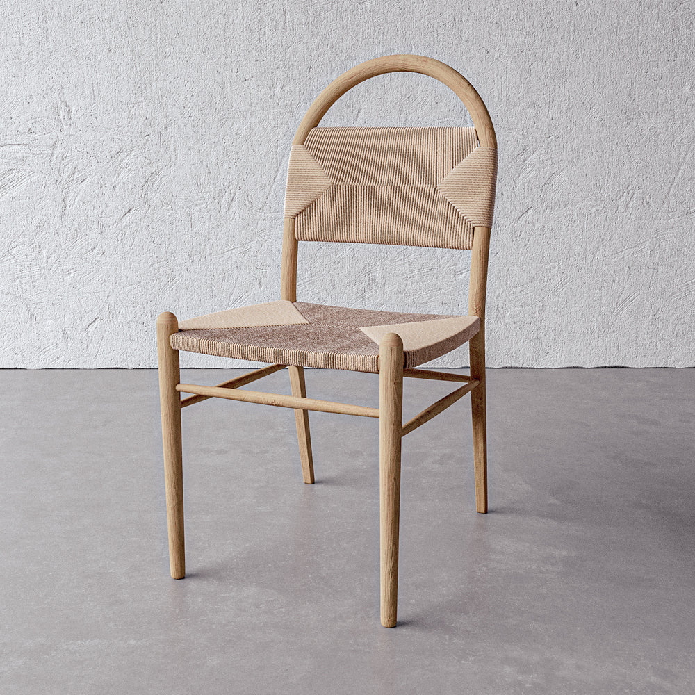 Lemieux et Cie Pernelle Dining Side Chair in oak with woven rush seat and arched back, shown on concrete floor against textured white plaster wall.