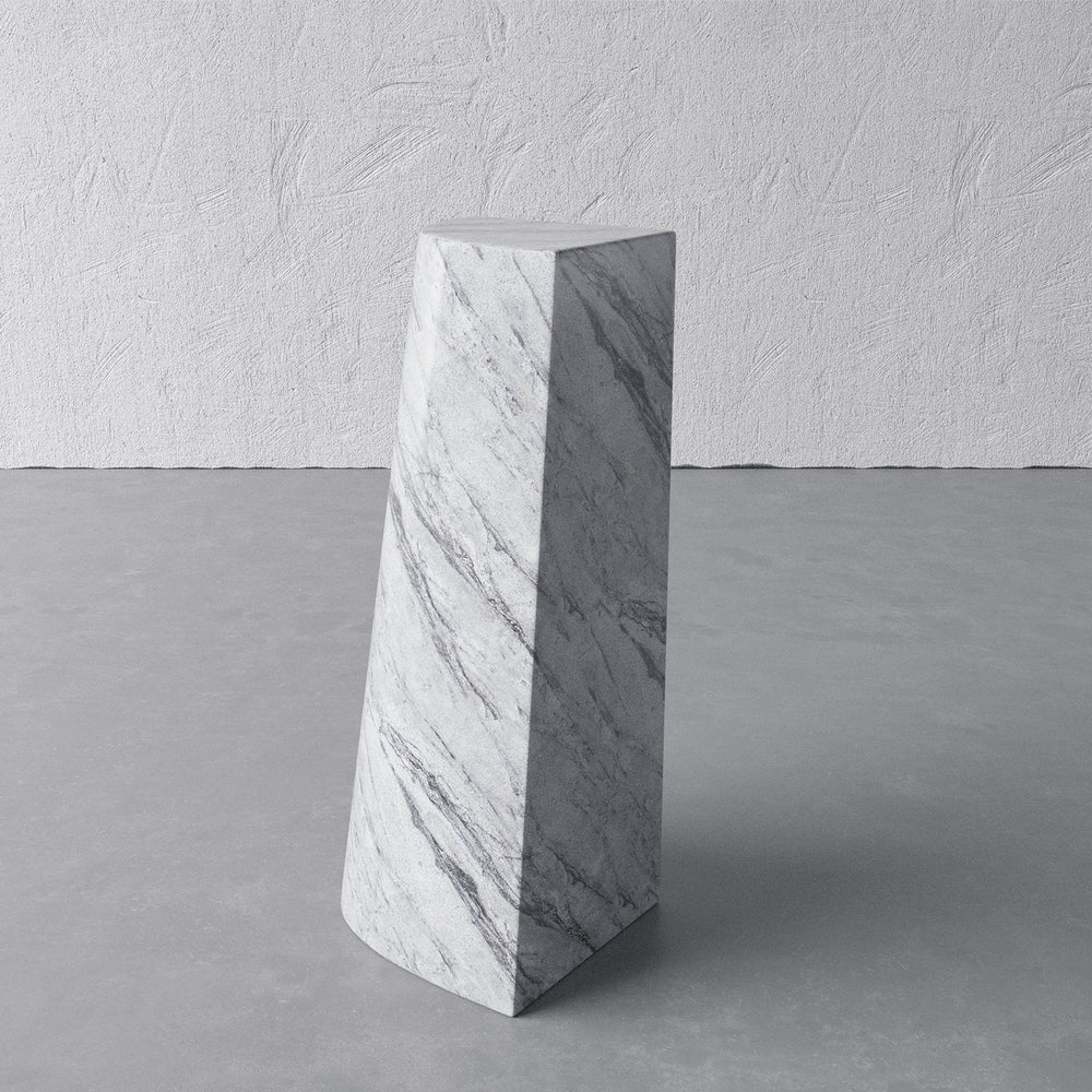 Lemieux et Cie Mille Pillar Side Table in blue forest marble, tapered geometric pedestal form on stone floor against textured plaster walls.
