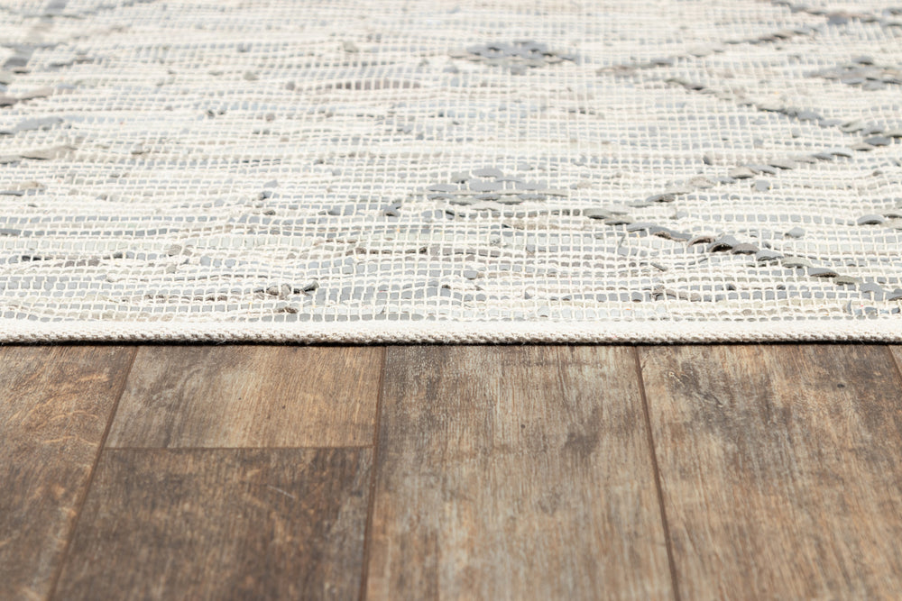 Lemieux et Cie Tézah rug in ivory and grey handwoven recycled leather, low-profile textured weave with organic dimensional pattern, shown on aged wood plank flooring.