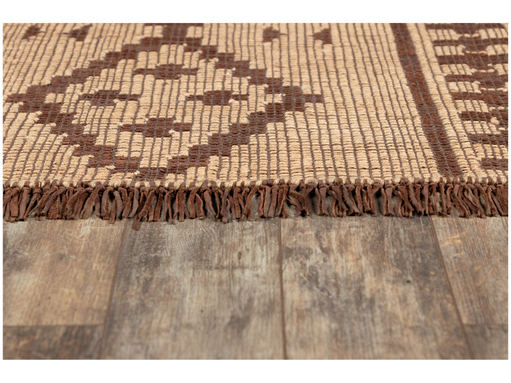 Lemieux et Cie Tugart Dagana Rug in natural and brown, handwoven leather and jute with fringed edge, shown on weathered wood flooring.
