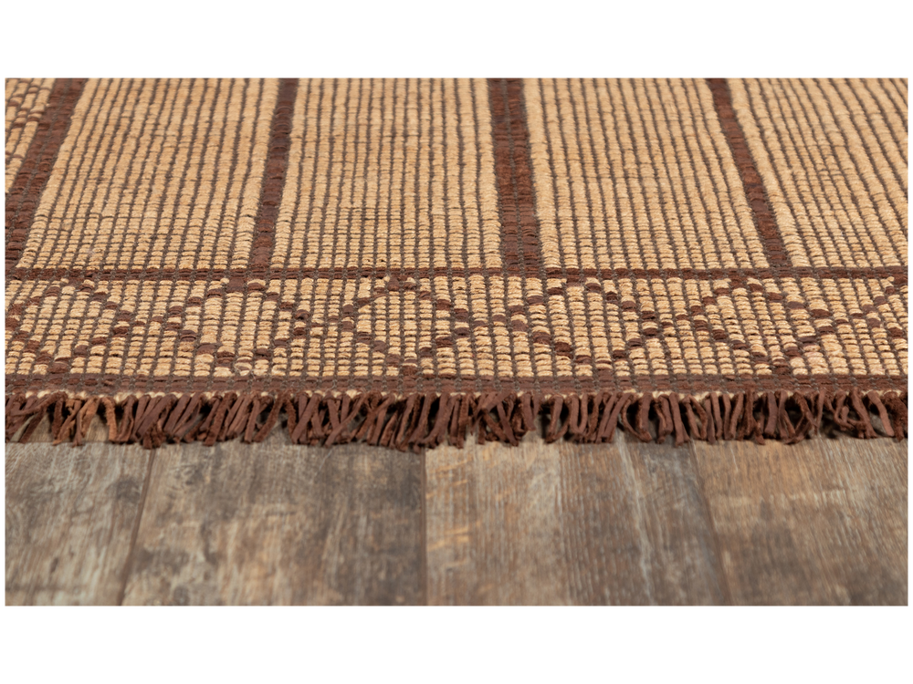 Lemieux et Cie Tugart Joma Rug in natural jute and leather, handwoven geometric rug with fringed edge, shown on weathered wood flooring.