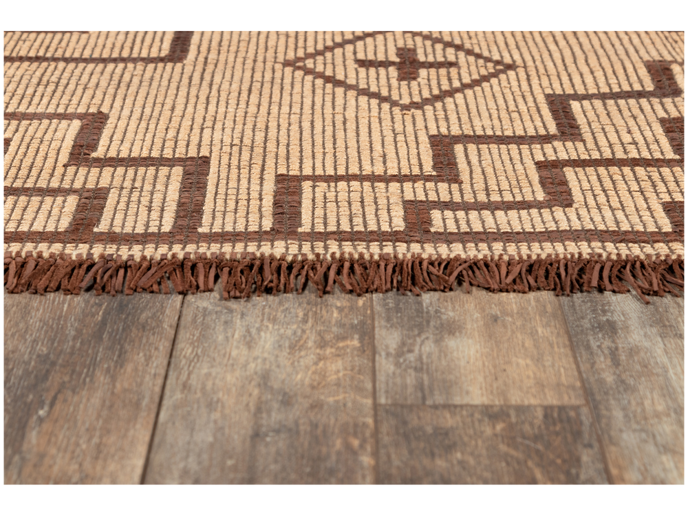 Lemieux et Cie Tugart Rug in natural jute and brown leather with geometric pattern and hand-knotted fringe, handwoven area rug shown on weathered wood flooring.