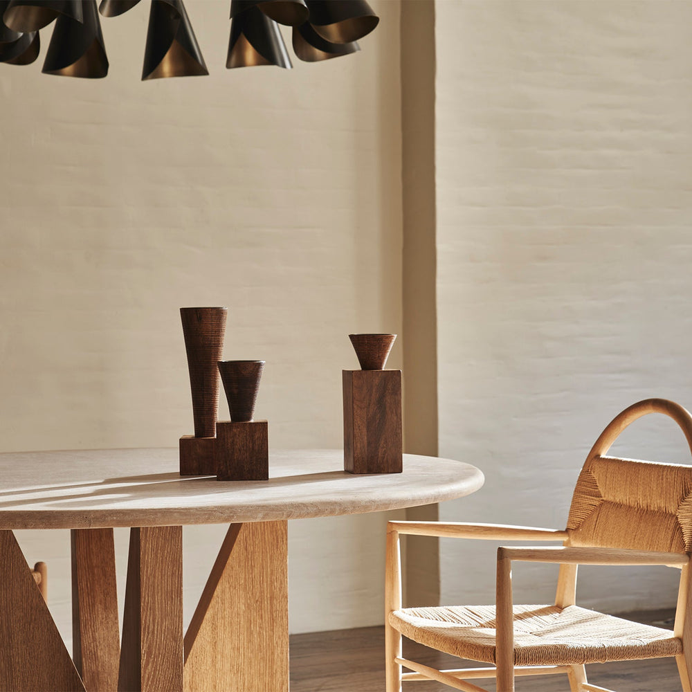 Lemieux et Cie Trio of Candleholders, handcrafted sculptural pedestals in dark warm tones, arranged on stone table beside woven chair in soft daylight.