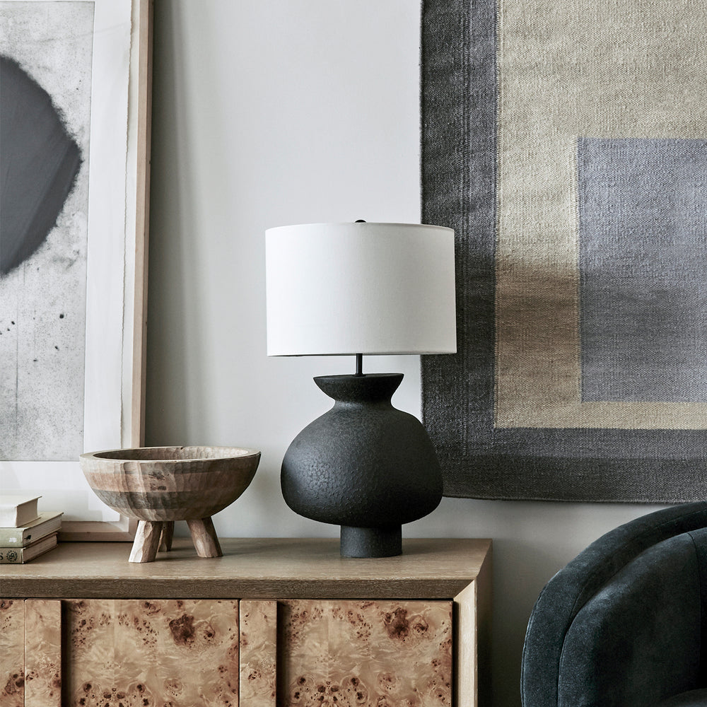 Lemieux et Cie Casis Lamp in matte black earthenware with white drum shade, sculptural table lamp on burl wood console beside framed art and woven textile