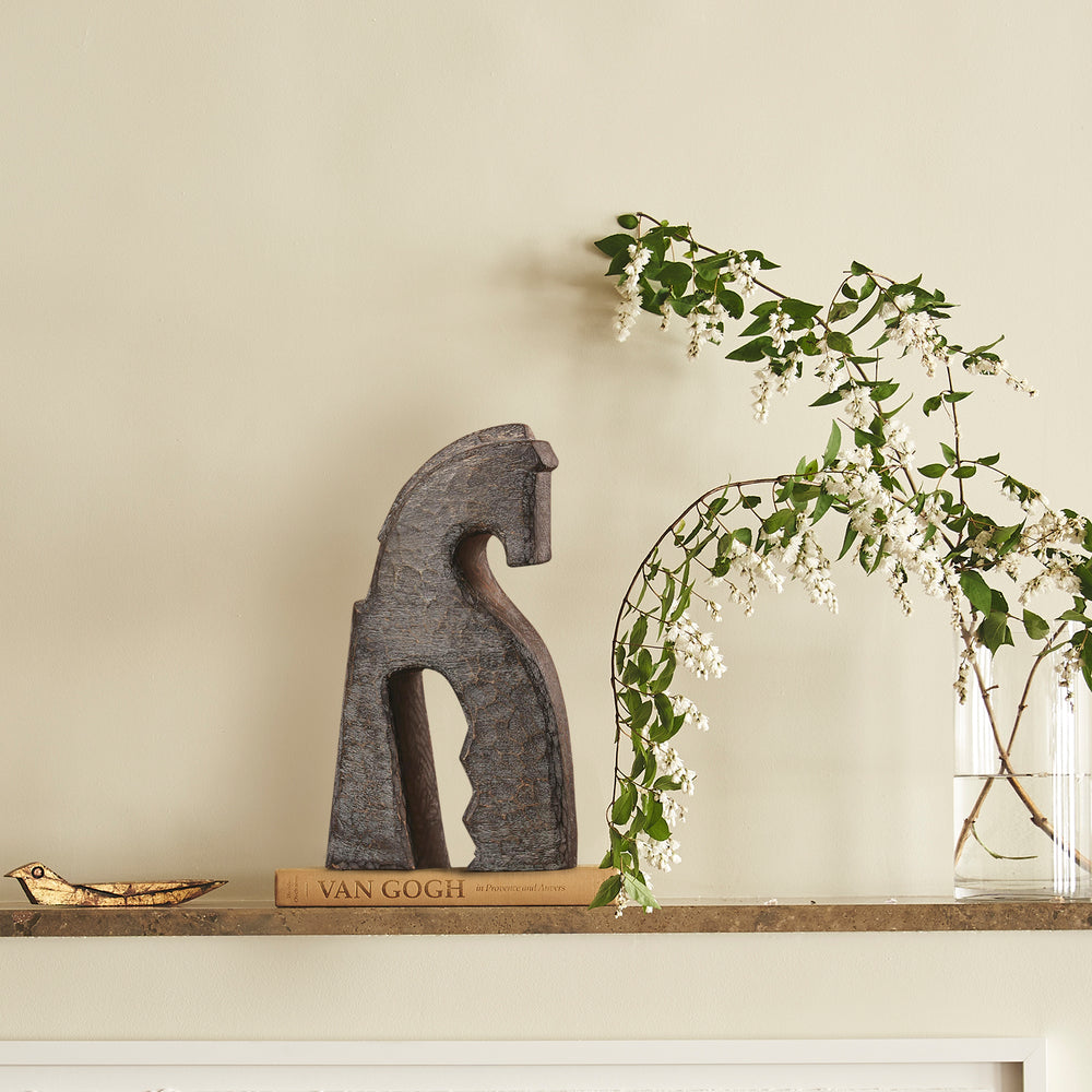 Lemieux et Cie Cheval Object, sculptural horse form, displayed on stone shelf with flowering branches and neutral walls in warm natural light.