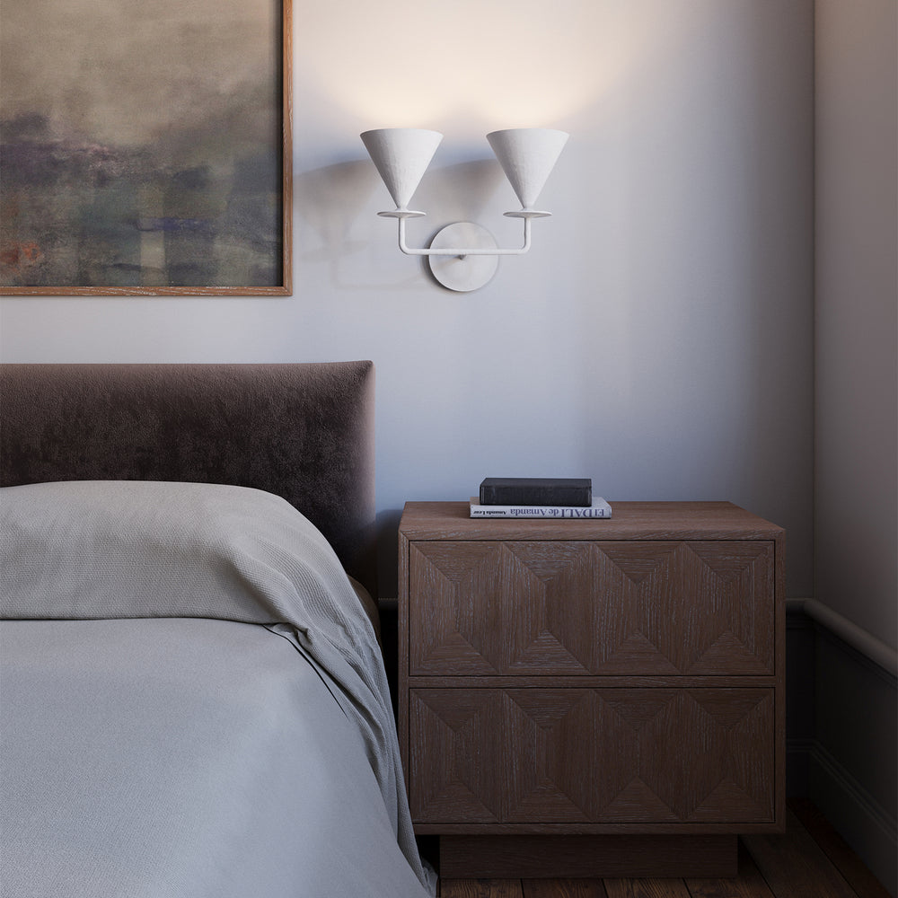 Lemieux et Cie Cornet Double Sconce, a designer lighting fixture mounted above a bedside table with two white plaster cone shades casting a soft glow.