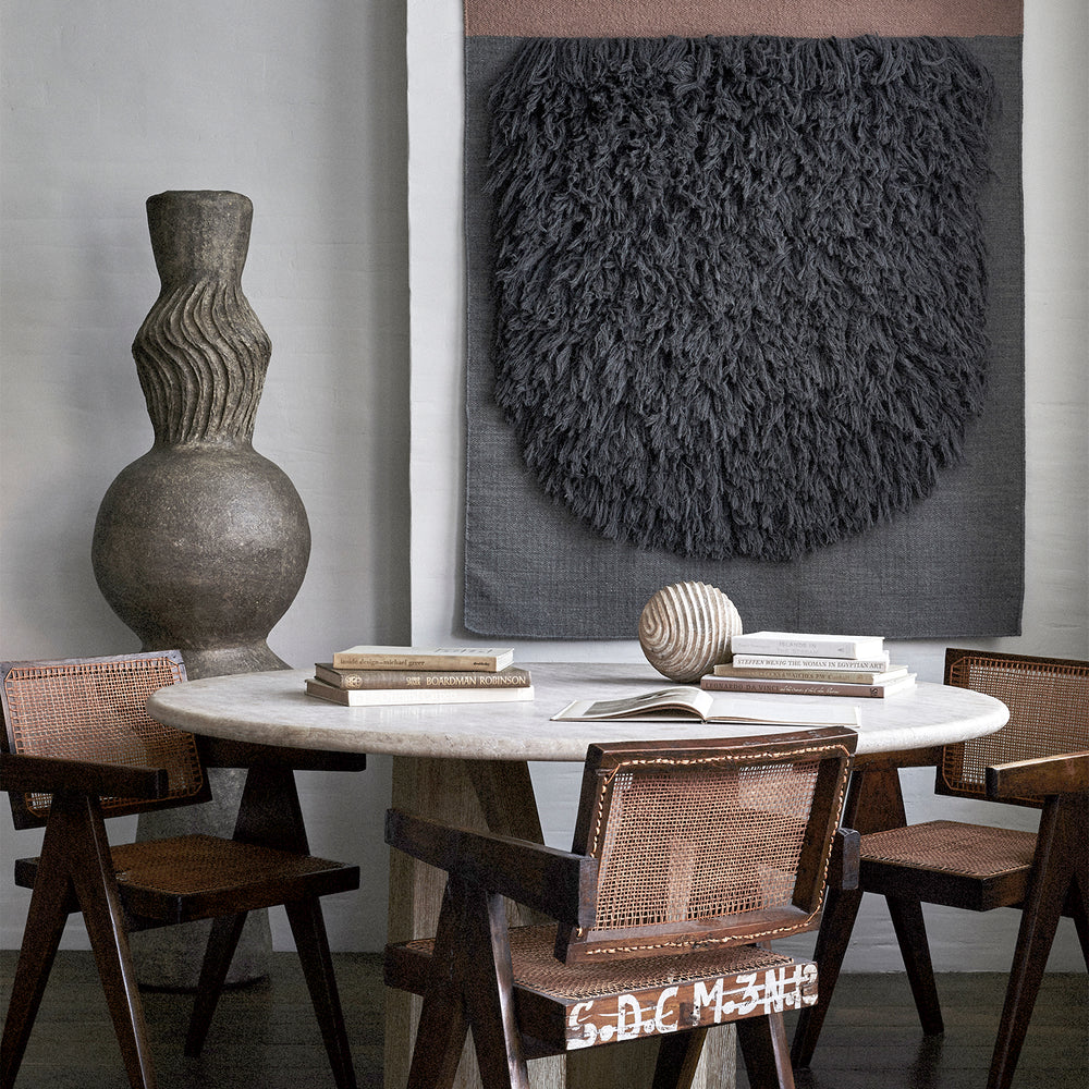 Lemieux et Cie Honore Totem, sculptural pillar with textured organic form, displayed on marble-top dining table with caned chairs in soft daylight.