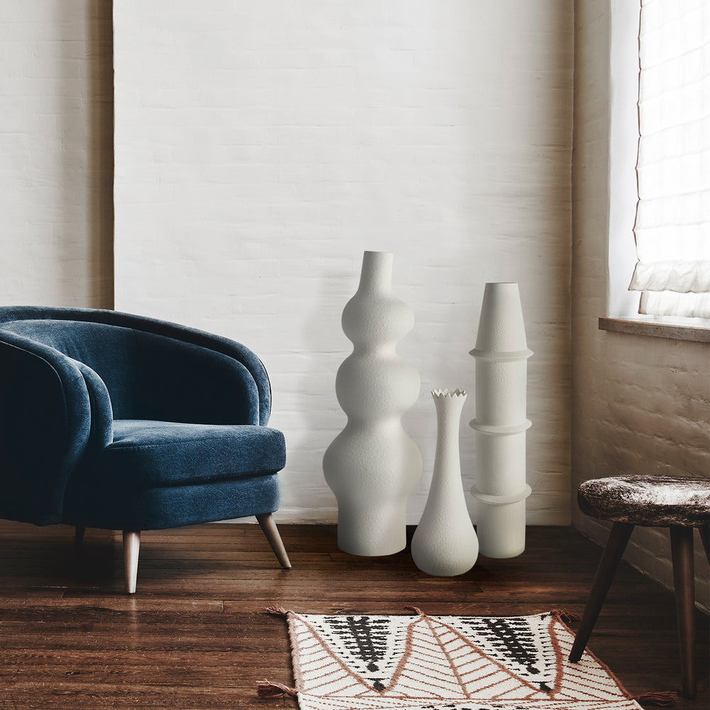Lemieux et Cie Panisse Vase in matte white, sculptural ceramic vase with organic stacked form, grouped with other vases beside a blue upholstered chair on wood floors.