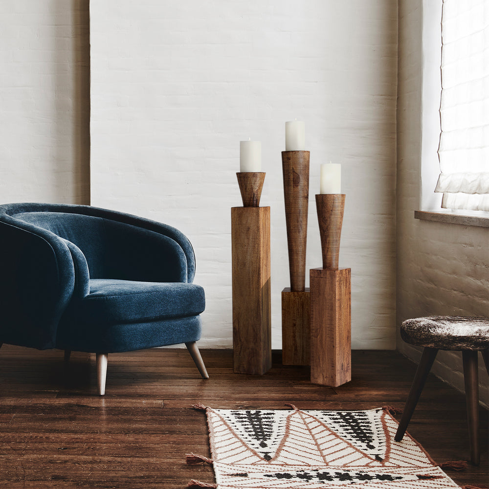 Lemieux et Cie Floor Pillar Candleholders, sculptural turned forms in varying heights with ivory candles, styled with blue velvet chair on wood floors.
